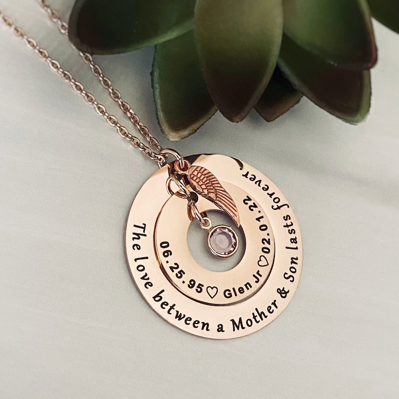 Mothers Bereavement necklace in rose gold and engraved with a memorial phrase. inside round hollow pendant is personalized with sons birthdate name and death date. Stone hangs in the center. Angel wing charm attached to the pendant and the chain.