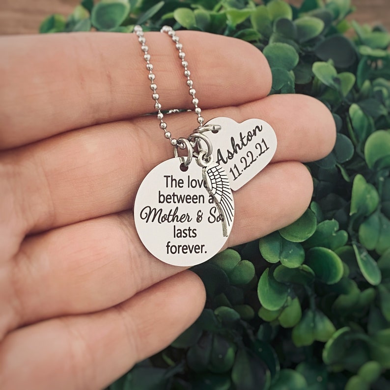 Puede incluir: Collar de plata con dos colgantes redondos. El colgante m&aacute;s grande tiene el texto "The love between a Mother & Son lasts forever." El colgante m&aacute;s peque&ntilde;o tiene forma de coraz&oacute;n y tiene el texto "Ashton 11.22.21".