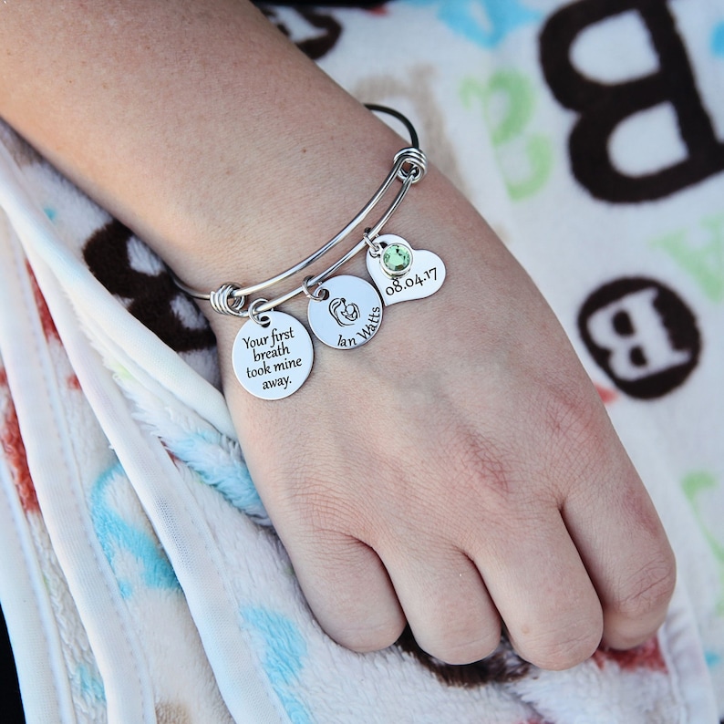 picture of woman holding a baby blanket wearing a mothers charm bracelet engraved with her child's name and date of birth
