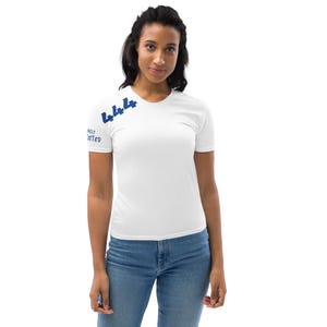 Könnte beinhalten: Ein weißes Kurzarm-T-Shirt mit der dunkelblauen Zahl 444, die diagonal auf dem oberen rechten Brustbereich aufgedruckt ist, und dem Text DIVINELY GUIDED in Dunkelblau auf dem rechten Ärmel, kombiniert mit einer blauen Jeans.