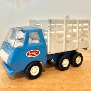 May include: A blue Tonka toy truck with a white metal bed and a white metal cage. The truck has a clear plastic cab and four black wheels.