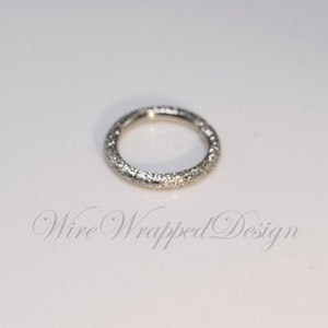 May include: A silver ring with a textured surface. The ring is a simple circle with no embellishments.