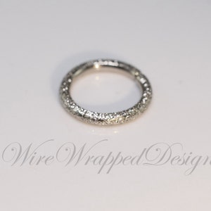 May include: A silver ring with a textured surface. The ring is a simple circle with no embellishments.