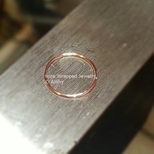 May include: A close-up of a thin, gold-colored wire ring on a metal surface. The ring is smooth and has a slight sheen. The text "Wire Wrapped Jewelry &copy; Azshy" is visible in the image.