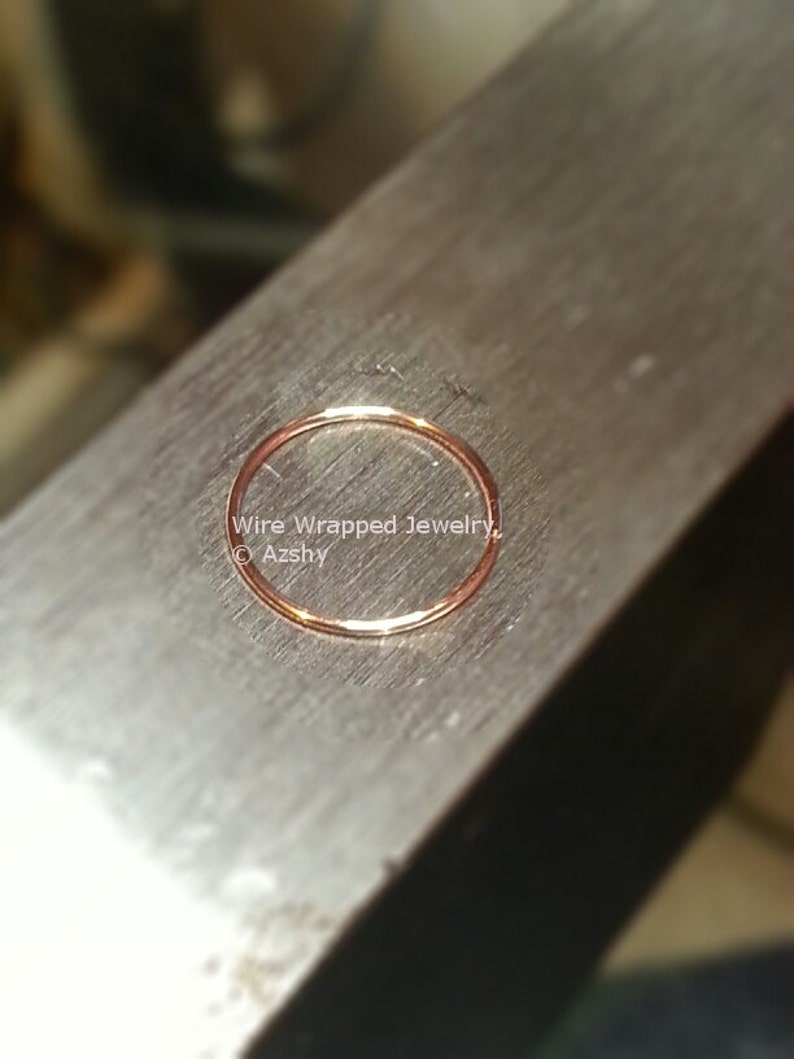 May include: A close-up of a thin, gold-colored wire ring on a metal surface. The ring is smooth and has a slight sheen. The text "Wire Wrapped Jewelry &copy; Azshy" is visible in the image.
