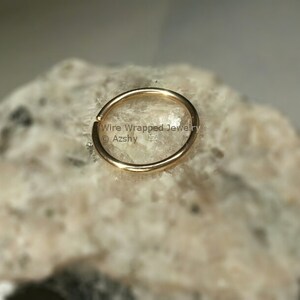 May include: A gold-colored hoop earring, shown on a rock background. The earring is a simple, circular design.  Wire Wrapped Jewelry &copy; Azshy