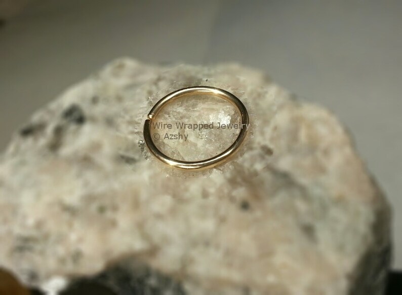 May include: A gold-colored hoop earring, shown on a rock background. The earring is a simple, circular design.  Wire Wrapped Jewelry &copy; Azshy