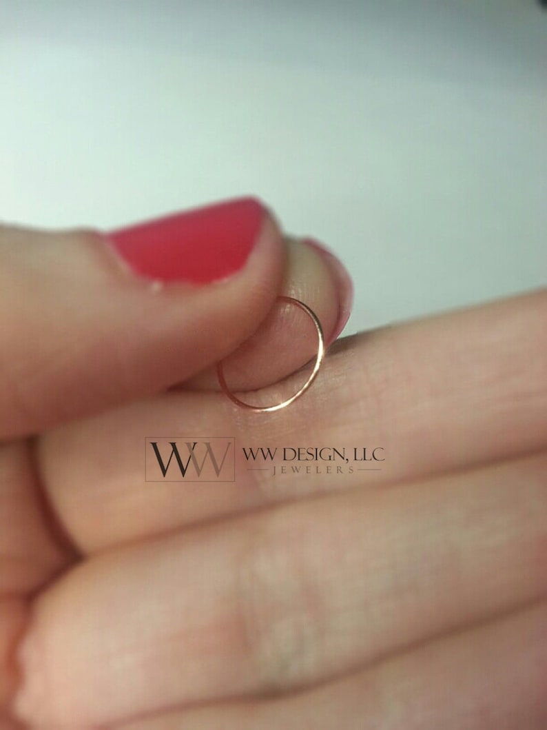 May include: A thin, gold-colored hoop earring. The earring is held in a person's hand.