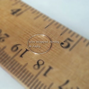 May include: A close-up of a thin gold nose ring, measured against a wooden ruler. The ring is approximately 1/8 inch in diameter. The text "Wire Wrapped Jewelry @Azshy" is visible in the image.