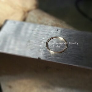 May include: A close-up of a gold ring on a metal surface. The ring is being worked on by a jeweler. The text "Wire Wrapped Jewelry @Azshy" is visible in the image.