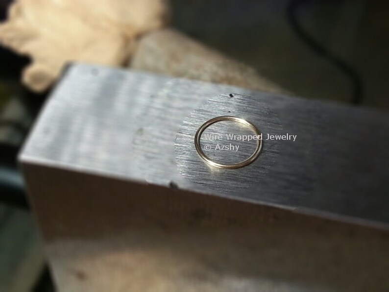 May include: A close-up of a gold ring on a metal surface. The ring is being worked on by a jeweler. The text "Wire Wrapped Jewelry @Azshy" is visible in the image.