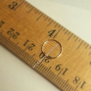 May include: A close-up of a gold nose ring hoop measuring 5/16 inch in diameter, placed on a wooden ruler. The ruler is marked with inches and fractions of an inch. The text "Wire wrapped jewelry &copy; Azsky" is visible on the ruler.