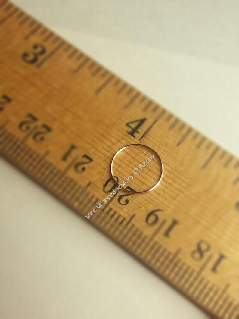May include: A close-up of a gold nose ring hoop measuring 5/16 inch in diameter, placed on a wooden ruler. The ruler is marked with inches and fractions of an inch. The text "Wire wrapped jewelry &copy; Azsky" is visible on the ruler.