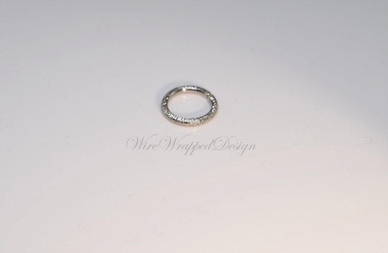 May include: A silver ring with a textured surface. The ring is a simple circle with no embellishments.