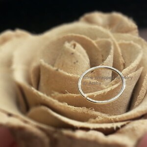 May include: A silver nose ring hoop on a beige rose. The text "Wire Wrapped Jewelry &copy; Azshy" is visible below the ring.