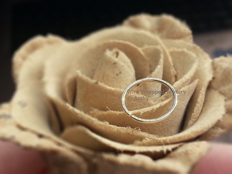 May include: A silver nose ring hoop on a beige rose. The text "Wire Wrapped Jewelry &copy; Azshy" is visible below the ring.