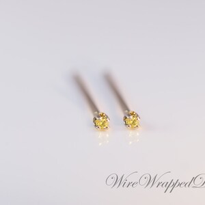 May include: A pair of small, yellow gemstone stud earrings with a silver setting. The earrings are on a white background.
