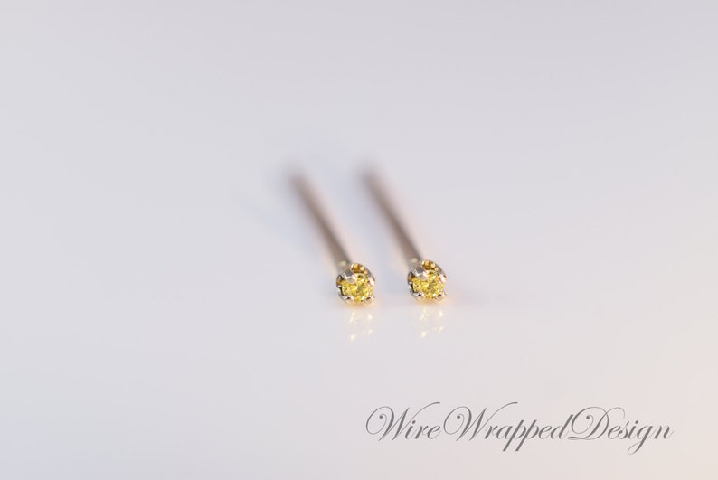 May include: A pair of small, yellow gemstone stud earrings with a silver setting. The earrings are on a white background.