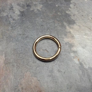 May include: A gold-colored metal ring, shown on a gray textured surface.