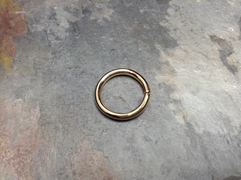 May include: A gold-colored metal ring, shown on a gray textured surface.