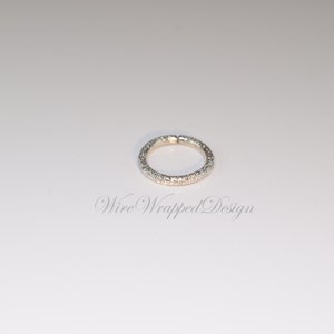 May include: A silver ring with a textured band of small, white stones.