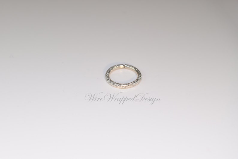 May include: A silver ring with a textured band of small, white stones.