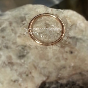 May include: A close-up of a gold-colored wire wrapped hoop earring. The earring is sitting on a white, textured surface. The text "Wire Wrapped Jewelry &copy; Azshy" is visible below the earring.