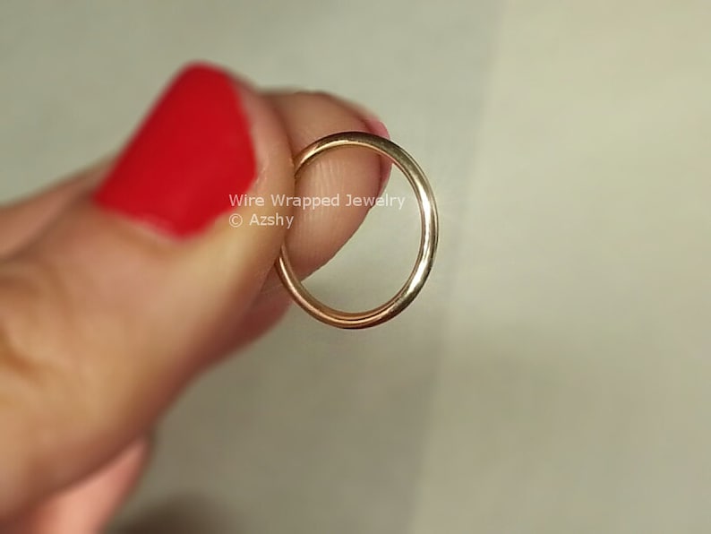 May include: A thin gold wire ring, held by a finger with red nail polish. The ring is simple and delicate, with a smooth, polished finish.  Wire Wrapped Jewelry &copy; Azzshy