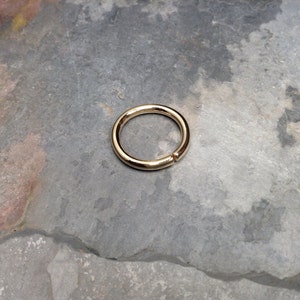 May include: A gold-colored seamless ring, likely made of metal, is shown on a gray, textured surface. The ring is circular and appears to be a simple, minimalist design.