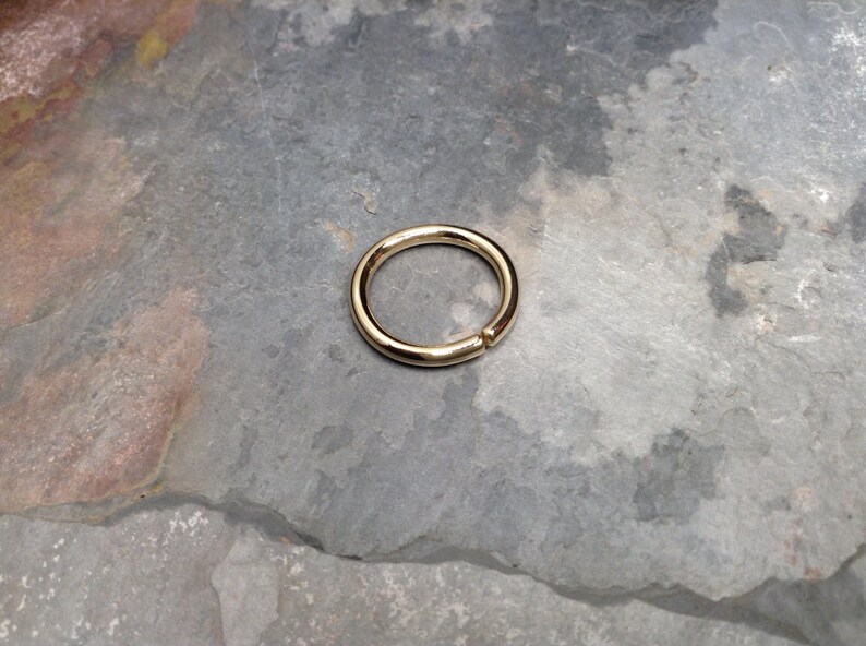 May include: A gold-colored seamless ring, likely made of metal, is shown on a gray, textured surface. The ring is circular and appears to be a simple, minimalist design.