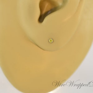 May include: A close-up of a yellow gemstone stud earring in a person's earlobe.