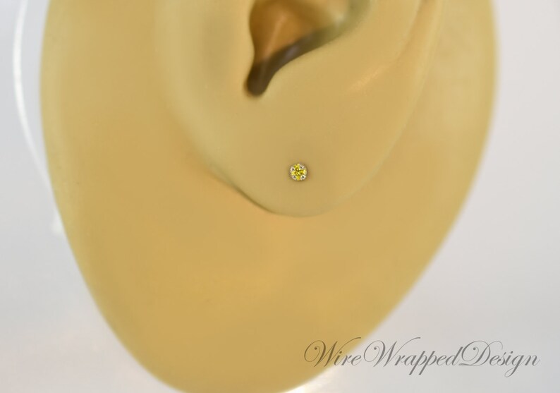 May include: A close-up of a yellow gemstone stud earring in a person's earlobe.