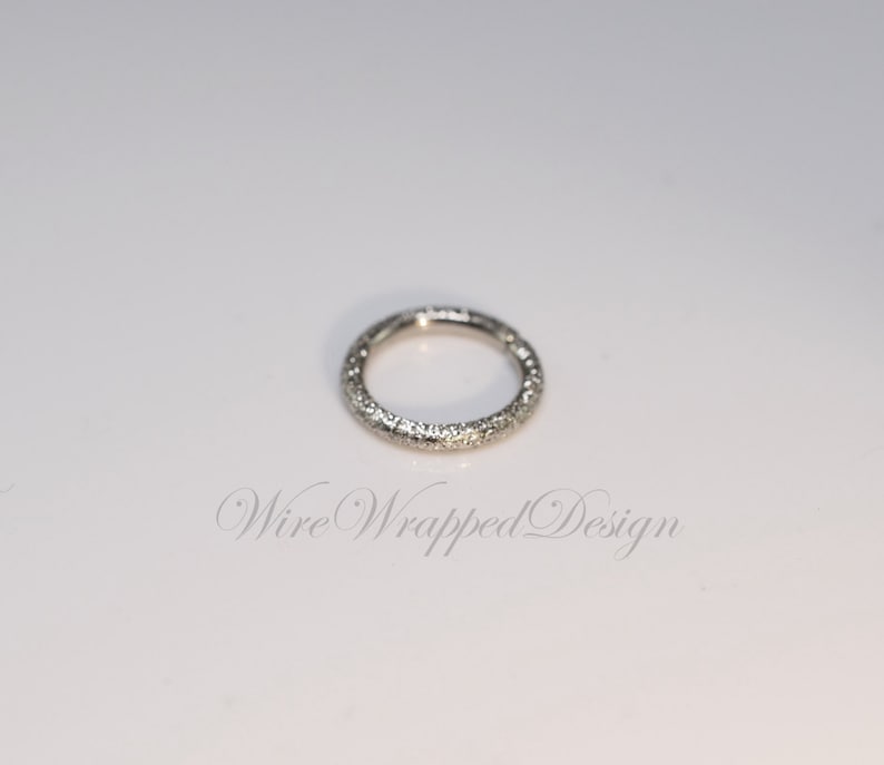 May include: A silver ring with a textured surface. The ring is a simple circle with no embellishments.