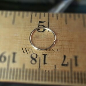May include: A gold nose ring hoop measuring 1/8 inch in diameter, placed on a wooden ruler for size reference.
