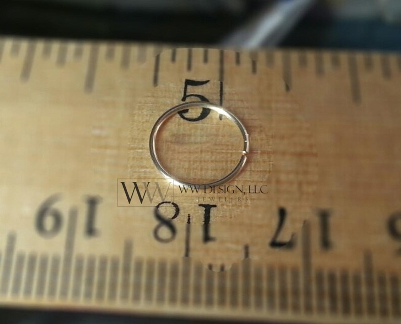 May include: A gold nose ring hoop measuring 1/8 inch in diameter, placed on a wooden ruler for size reference.