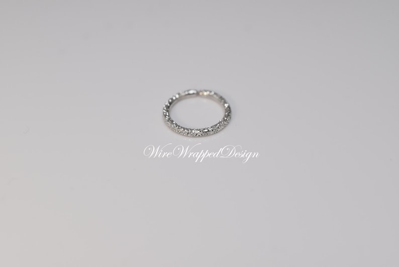 May include: A silver band ring with a row of small, clear stones set around the entire band. The ring is on a white background. "Wire Wrapped Design" is written in cursive below the ring.