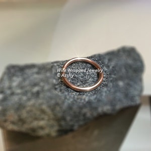 May include: A close-up of a rose gold wire ring on a grey textured surface. The text "Wire Wrapped Jewelry &copy;Azshy" is visible below the ring.