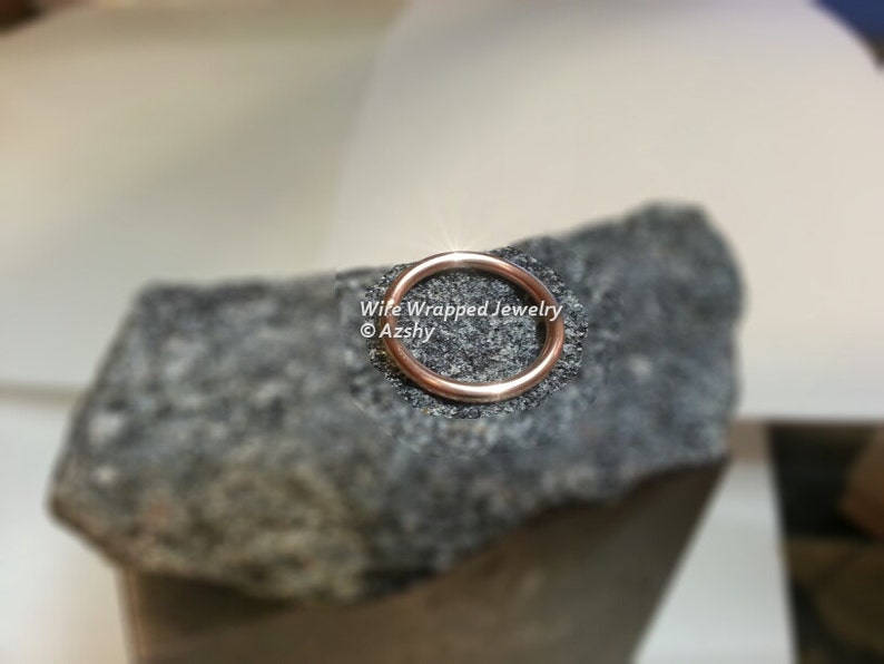 May include: A close-up of a rose gold wire ring on a grey textured surface. The text "Wire Wrapped Jewelry &copy;Azshy" is visible below the ring.