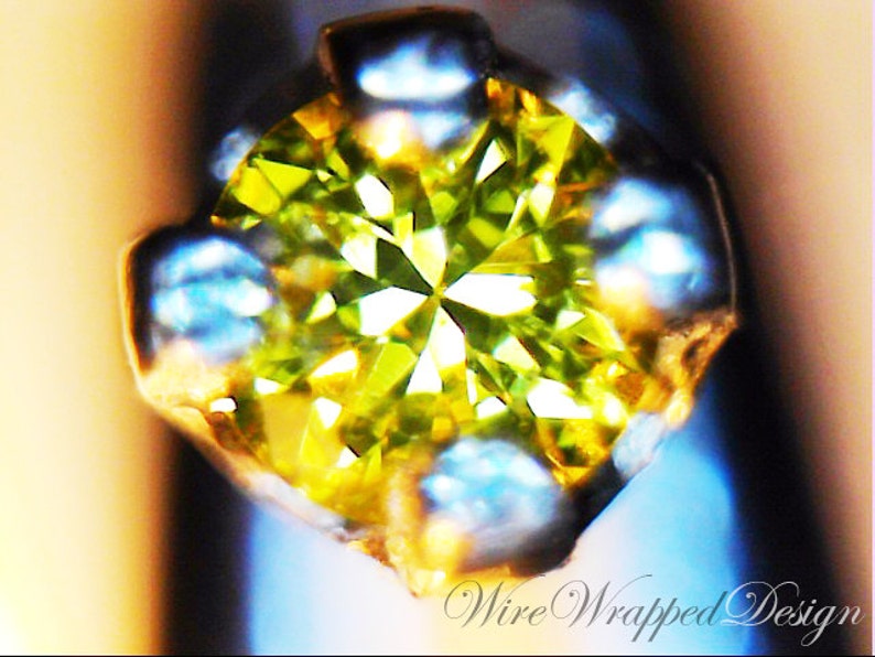 May include: A close-up of a green gemstone set in a silver prong setting. The gemstone is faceted and has a bright, sparkling appearance.