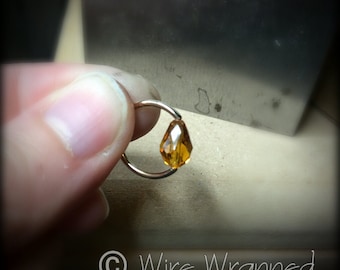 May include: A gold wire wrapped ring with a teardrop-shaped amber gemstone.