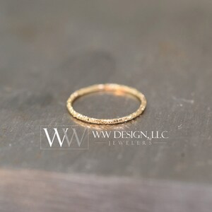 May include: A thin gold band ring with a textured surface.