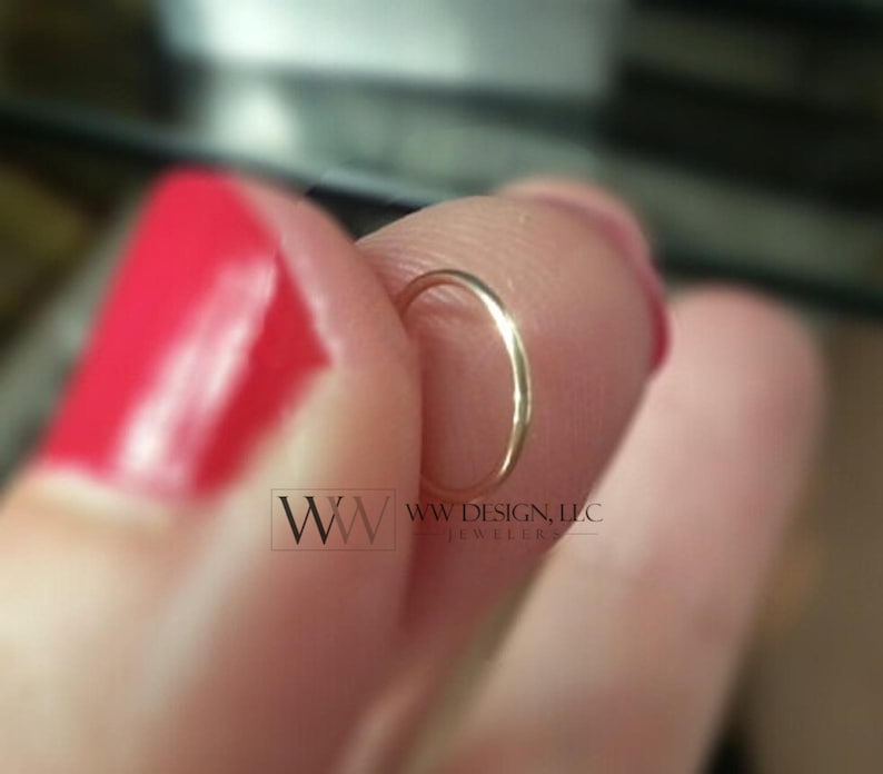 May include: A gold nose ring hoop, held between a finger and thumb.