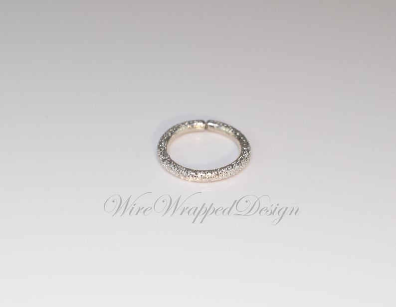 May include: A silver ring with a textured surface. The ring is a simple circle with no embellishments.