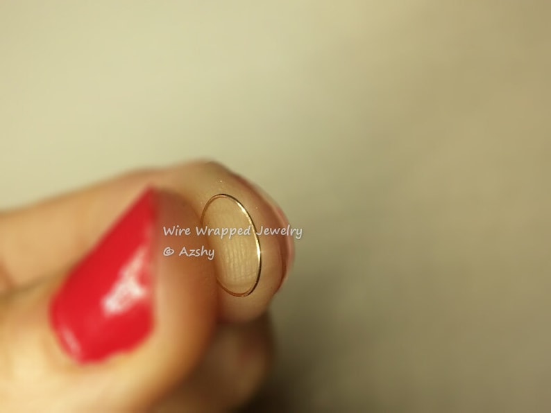 May include: A close-up of a gold wire wrapped hoop earring. The earring is held between two fingers. The text "Wire Wrapped Jewelry @Azshy" is visible in the image.