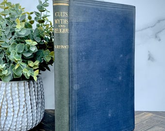 May include: A hardback book titled Cults, Myths and Religions by S. Reinach with a dark blue cover and a green spine featuring gold lettering. The book is positioned upright, displaying the front cover and the spine clearly.