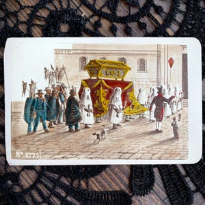 May include: A vintage postcard illustration depicting a religious procession on a cobblestone street. A golden casket is carried under a red and gold canopy by figures in white hooded robes. Other figures in dark coats and hats follow, with the text No. 2775.
