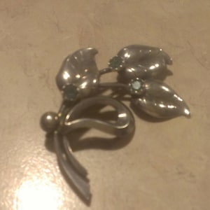 Puede incluir: Broche de plata con forma de flor con tres piedras verdes.