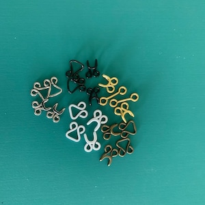 Pode incluir: Conjunto de fechos de gancho e olho de metal e plástico em dourado, preto e branco.