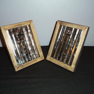 May include: Two rustic wood picture frames with a silver metallic finish. Each frame has a metal clip on the top.