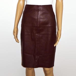 May include: A high-waisted, knee-length skirt in a deep burgundy color. The skirt features a smooth, solid-colored finish with a vertical seam running down the center front and a horizontal seam across the upper hip area, creating a structured silhouette.